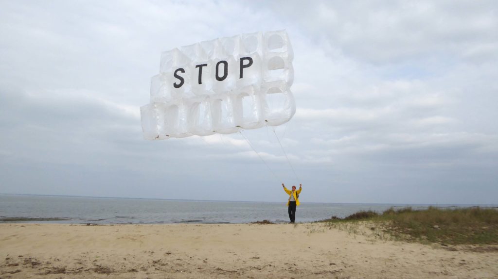 Thomas Lanfranchi, élevant une forme volante sur une plage. Le mot STOP est inscrit dans le ciel.